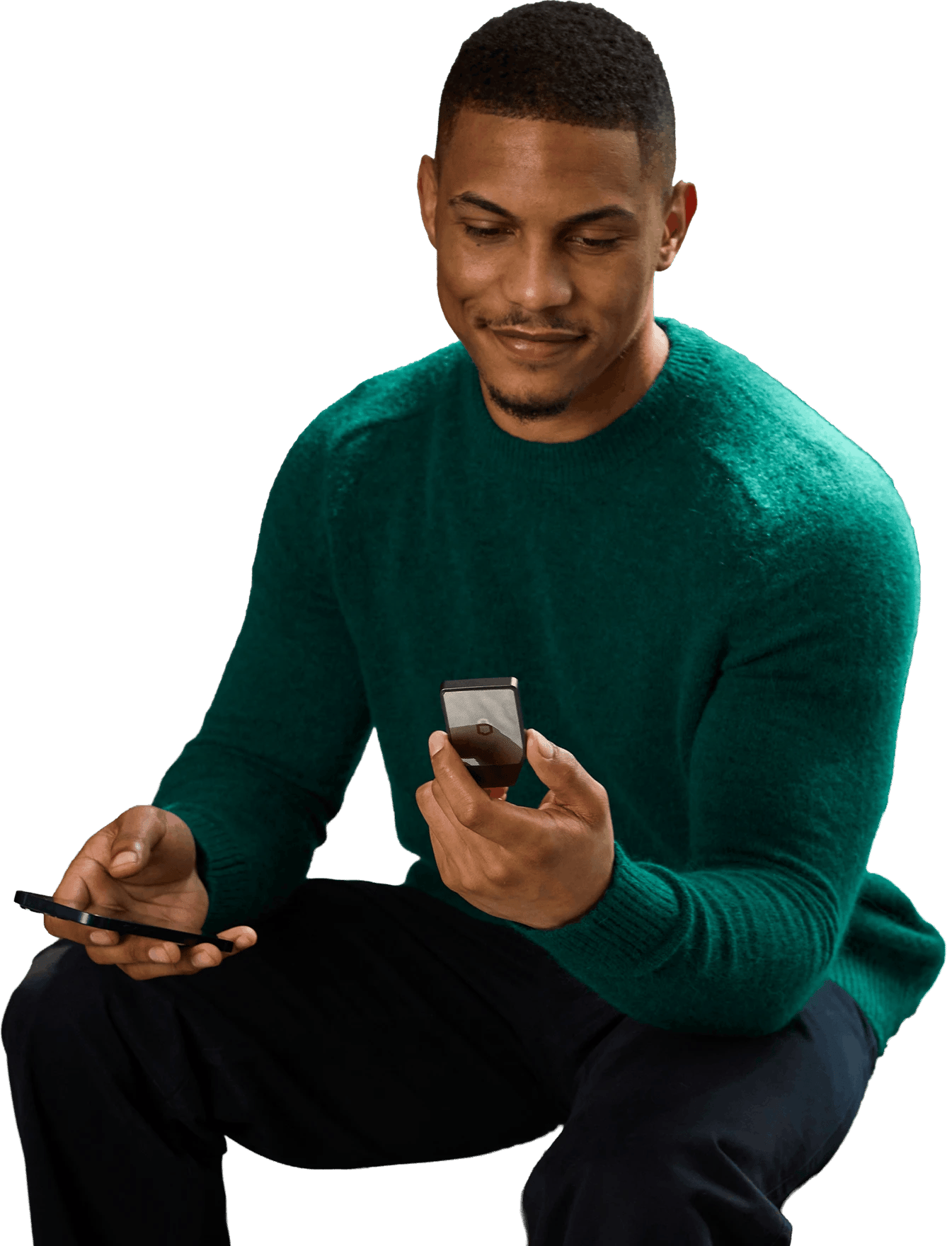Man in a green sweater sitting and smiling while holding a Trezor Safe 7 hardware wallet and a smartphone.